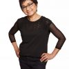 Sophisticated woman in black lace and sheer sleeve top, smiling confidently, standing against a white background, showcasing elegance, fashion, and confidence.