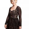 Elegant woman wearing a black lace dress with intricate floral patterns and sheer long sleeves, suitable for fashionable events and stylish occasions.
