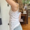 Bright woman wearing a white sleeveless top and denim jeans, standing indoors with natural background, highlighting casual style and comfortable fashion choices.