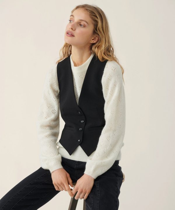 Soft cream knit sweater with eyelet detailing paired with a tailored black vest, stylish and cozy fall fashion look.
