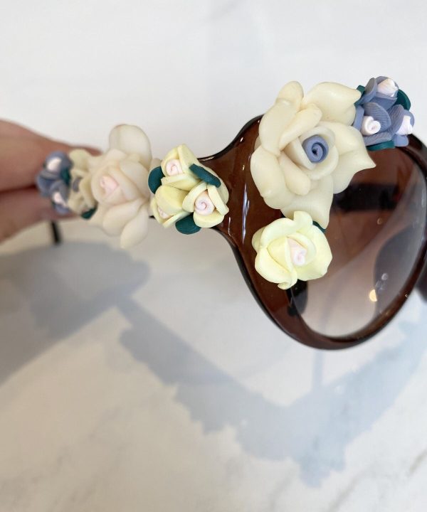 Cream-colored and blue fondant floral decorations on a glass and brown plastic decorative vase for floral art or cake toppers.