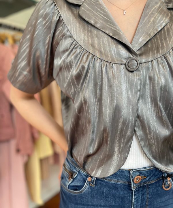 Silky satin blouse with a decorative ring detail on the collar, puffed short sleeves, paired with classic blue jeans, showcasing stylish women's fashion and elegant casual wear.