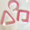 Pink marbled resin geometric shapes for jewelry or decor, including a circle, triangle, and square, on a white surface.