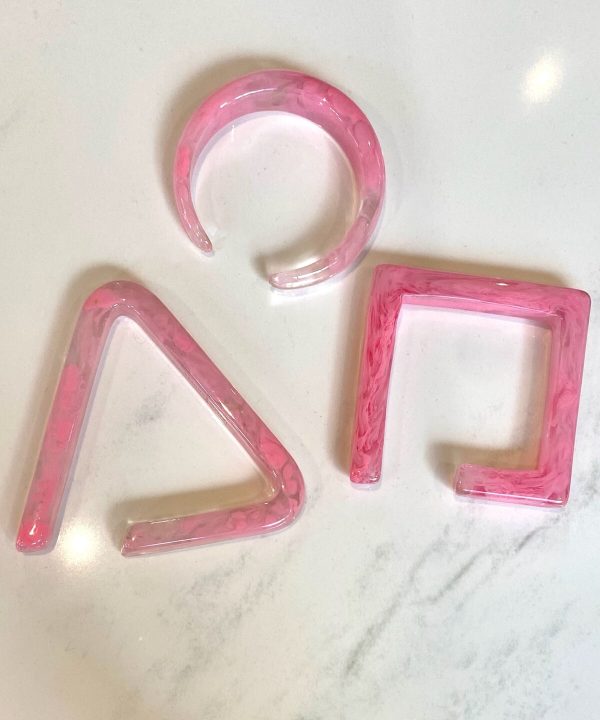 Pink marbled resin geometric shapes for jewelry or decor, including a circle, triangle, and square, on a white surface.