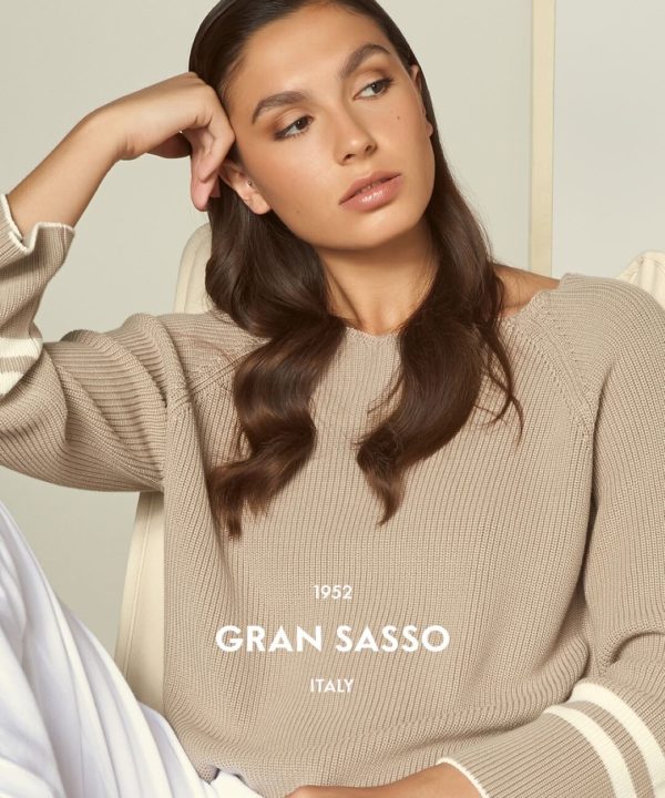Soft beige knit sweater fashion portrait of a young woman with long wavy brown hair, natural makeup, and thoughtful expression, representing stylish casual wear from Italy, brand Gran Sasso.