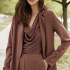 Elegant woman in brown tailored pantsuit and matching draped top, outdoor park setting, fashion photography, stylish professional attire, modern business look, katyamaker clothing collection.
