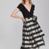 Black V-neck top paired with a high-waisted black and white striped midi skirt featuring a bow tie detail, stylish and contemporary fashion ensemble.