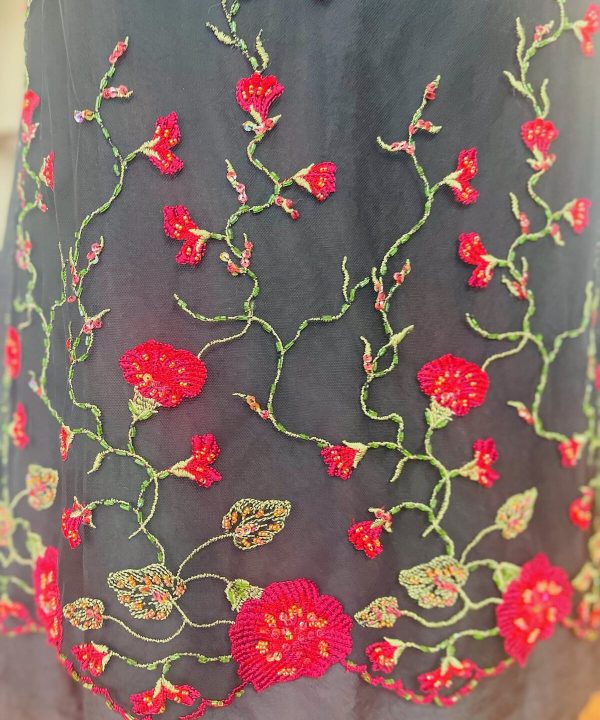 Luxurious black fabric featuring intricate red floral embroidery with green vine details, showcasing expert craftsmanship and delicate beadwork, perfect for elegant apparel and special occasions.
