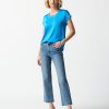 Bright blue satin blouse with v-neck and crisscross detail, paired with casual high-waisted jeans and clear heels, styled for a modern, chic look.