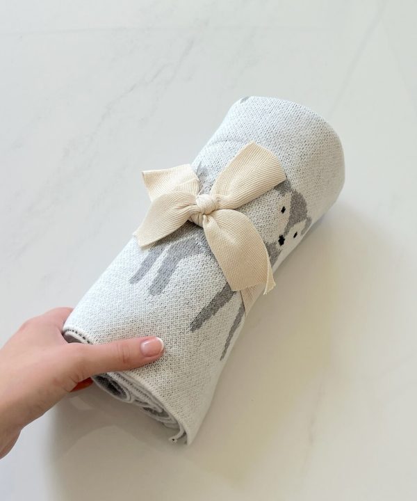 Hand-knit baby blanket with adorable deer design and cream-colored bow, perfect for nursery decor and baby gift ideas.