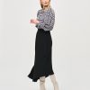 Black and white patterned blouse with bow tie detail, paired with a high-waisted black skirt and beige knee-high boots, fashion styling by Katya Maker, modern chic women's outfit, versatile for work or casual settings.