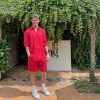 Bright young man in vibrant red casual summer outfit standing outdoors surrounded by lush greenery and ivy-covered walls, showcasing stylish fashion for a relaxed garden setting, ideal for lifestyle and fashion blogs.