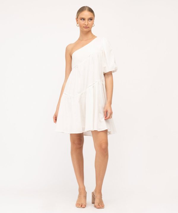 Flowy white one-shoulder dress with puff sleeve and ruffle hem, perfect for summer or beach occasions, styled with nude heels and jewelry for a chic, effortless look.