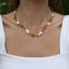 Golden amber and white baroque pearl necklace on a woman wearing a white top, close-up jewelry photo, handcrafted jewelry, natural stone necklace, elegant jewelry accessories.
