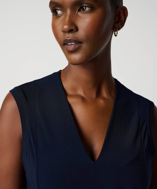 Sleek navy sleeveless dress on confident model with short hair and hoop earrings, fashion photography, modern style, elegant outfit, minimalistic background, high-quality image, professional fashion shot.