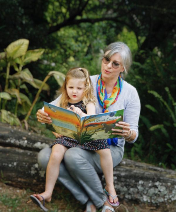Reading book with grandmother and granddaughter outdoors in nature, promoting family bonding, literacy, and outdoor activities, sunny day, lush green background, children’s storybook, learning, nature exploration, bonding with family, outdoor reading, educational activities, storytime.