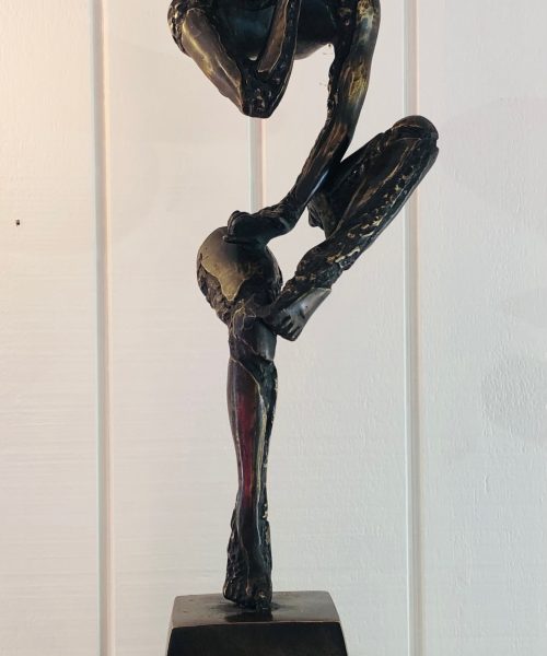 Contemporary bronze sculpture of a thinker in a crouching pose, focusing on creativity and artistic expression, displayed on a wooden surface with a plain background.