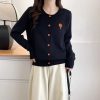 Cute black cardigan with orange button accents and an embroidered flower design, perfect for casual chic outfits and layering.