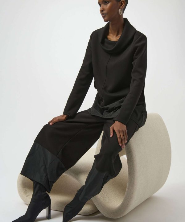 Elegant black fashion outfit featuring a stylish cowl neck top, wide-leg pants with tonal accents, and sleek pointed high-heel boots, styled in a minimalist studio setting.