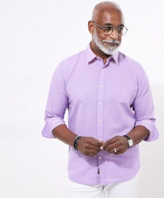 Elegant senior man wearing a lavender dress shirt, glasses, and stylish accessories, posing for a professional photoshoot for Katya Maker, emphasizing fashion, style, and confidence in men’s apparel.