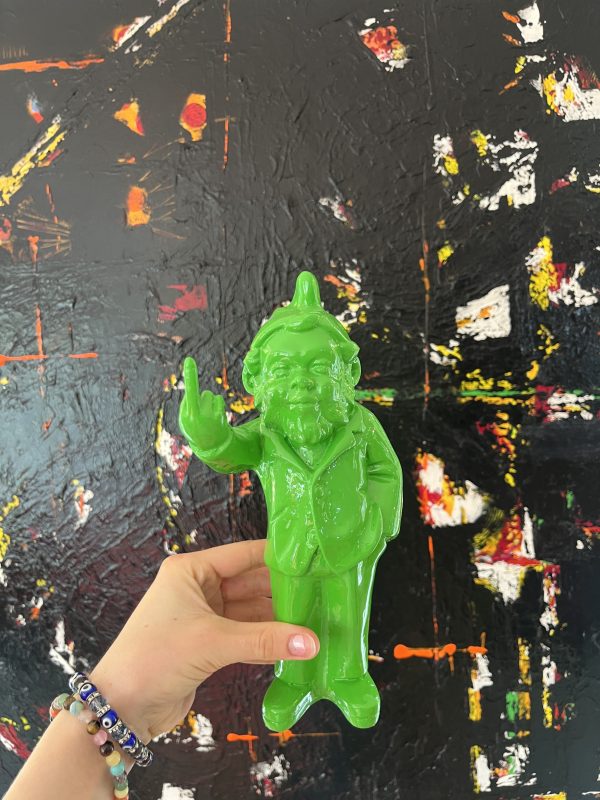 Colorful green resin sculpture of a quirky man with a raised middle finger, set against an abstract textured black background with splashes of red, yellow, and white paint.