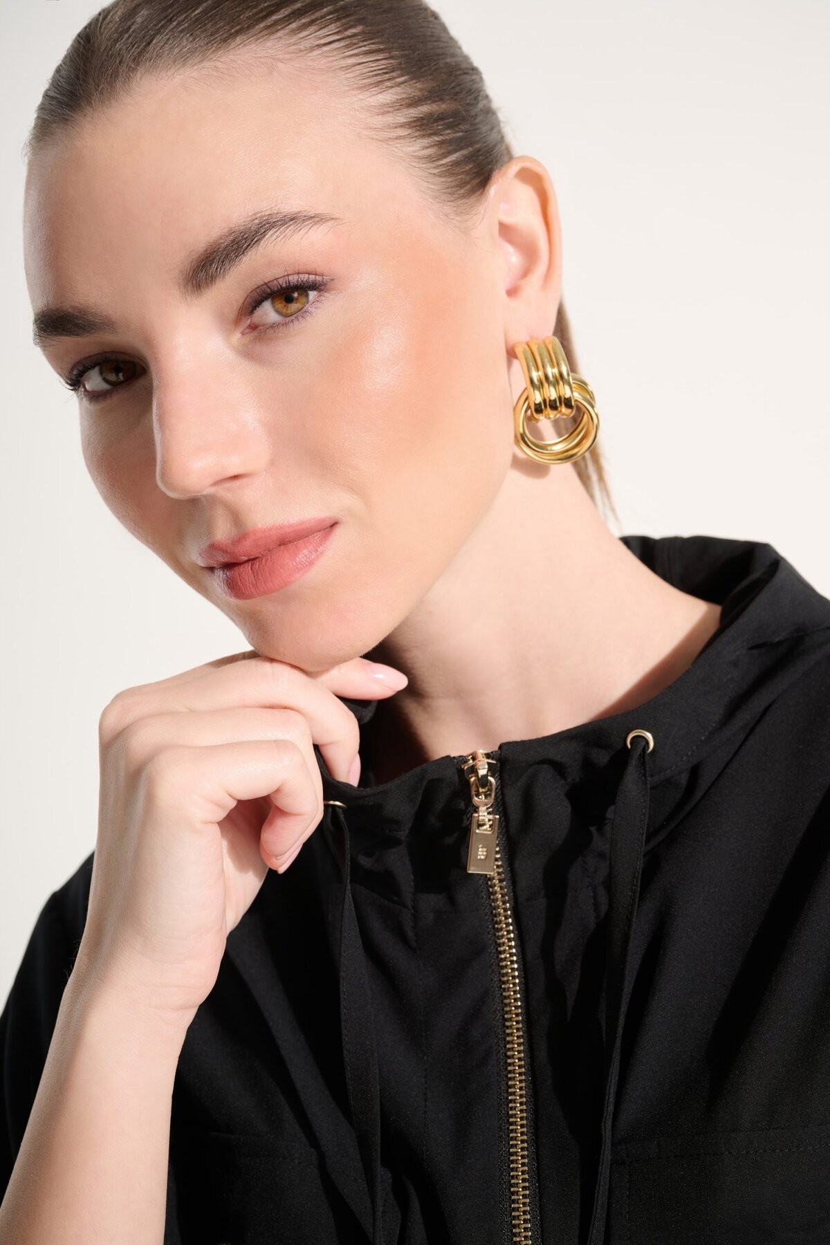 Elegant woman wearing statement gold earrings and a black hoodie, showcasing contemporary jewelry design and fashion accessories. Perfect for stylish, modern jewelry enthusiasts.
