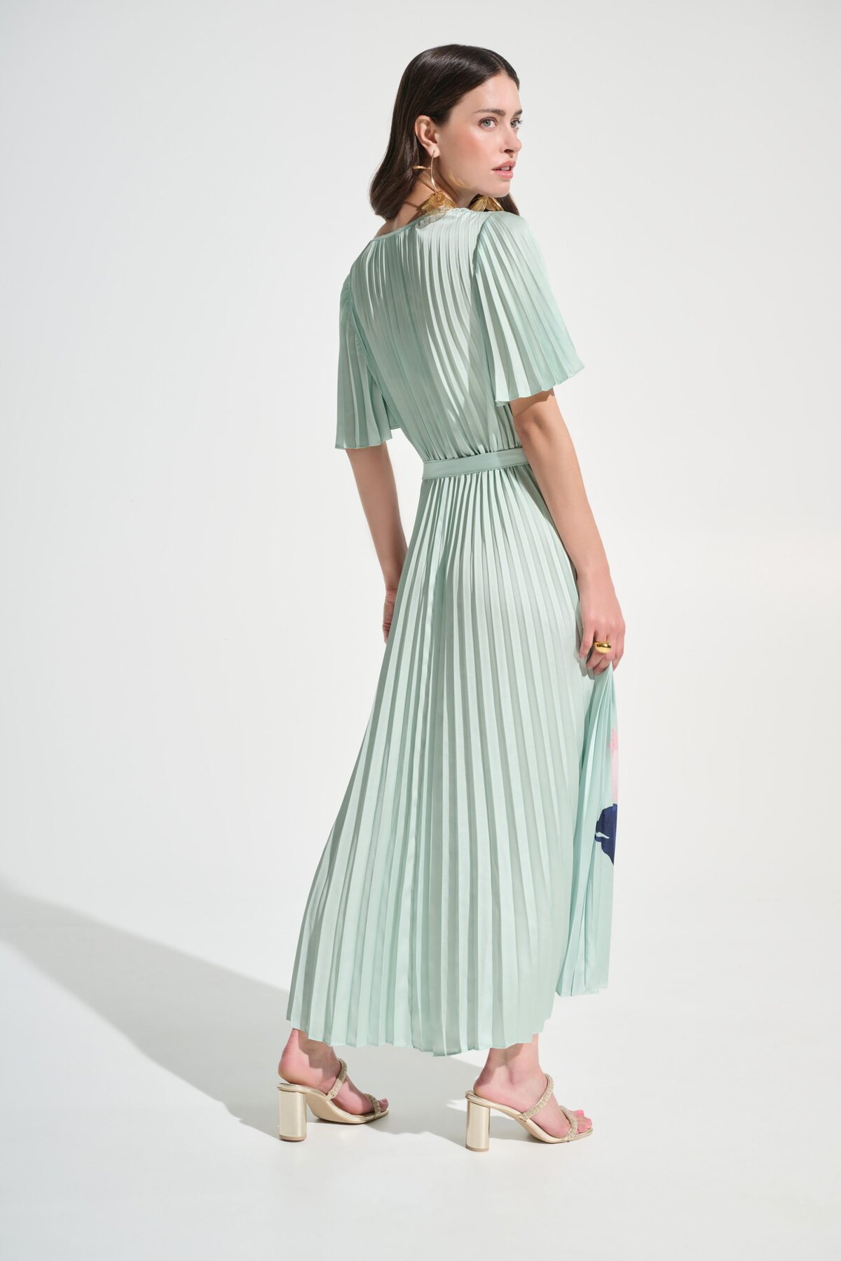 Soft mint green pleated midi dress with short sleeves and a waist tie, styled with nude heels, perfect for stylish summer or cocktail events.