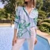 1. Stylish woman wearing a blue and green floral print shirt, white pants, and eco-friendly sunglasses by the poolside on a sunny day, showcasing fashion from katyamaker.