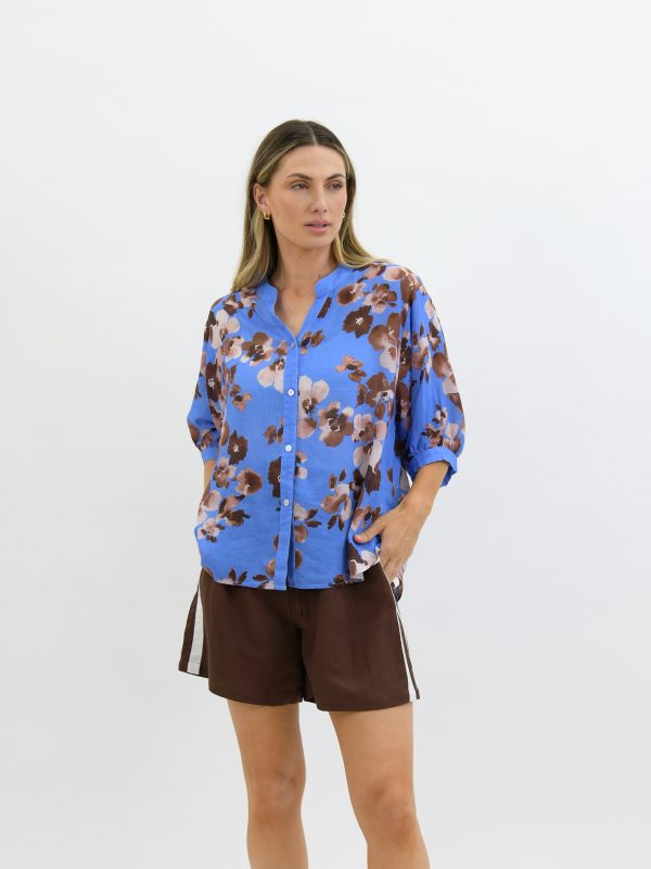 Elegant blue floral blouse with a relaxed fit, paired with brown shorts for a stylish summer look, perfect for casual outings and outdoor events.