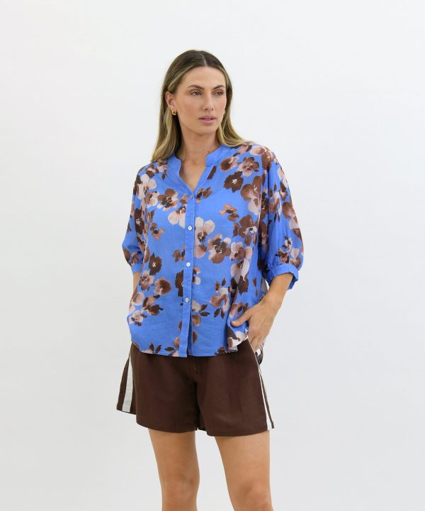 Elegant blue floral blouse with a relaxed fit, paired with brown shorts for a stylish summer look, perfect for casual outings and outdoor events.